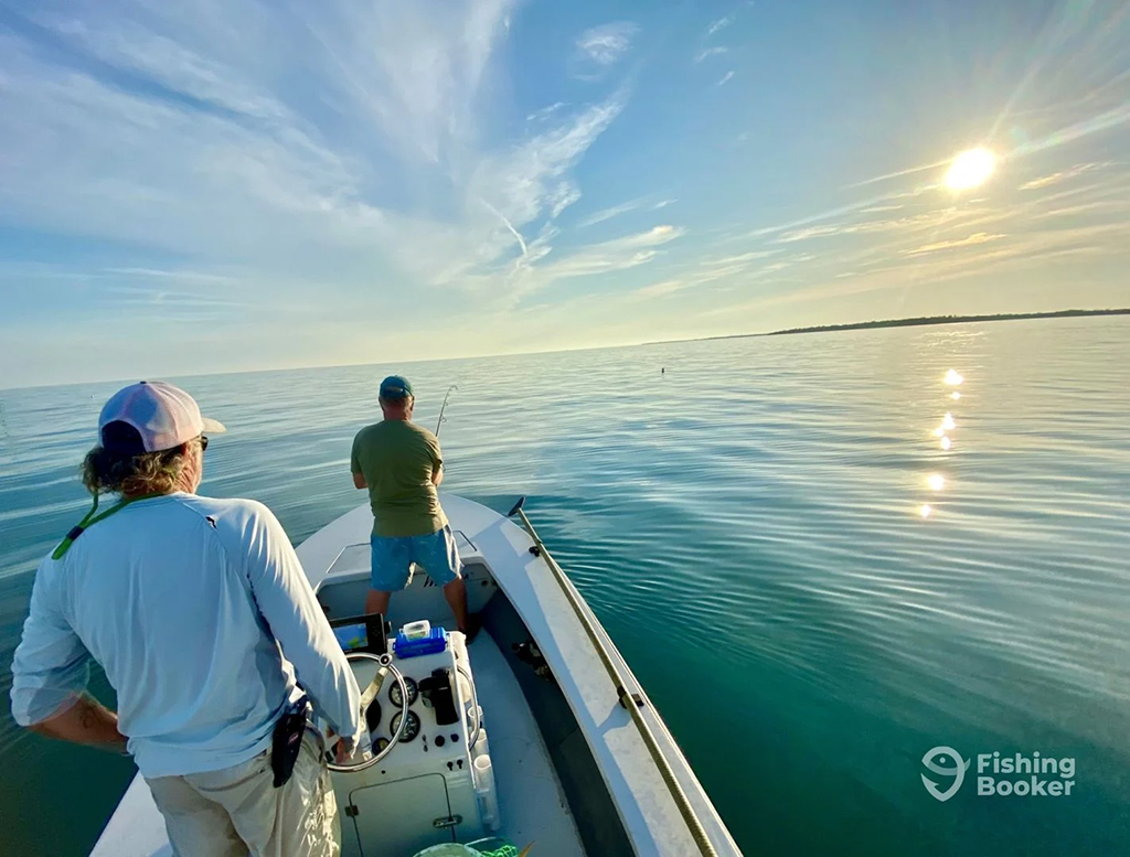Two anglers ride a boat across the flats as the sun rises over an island at Key West
