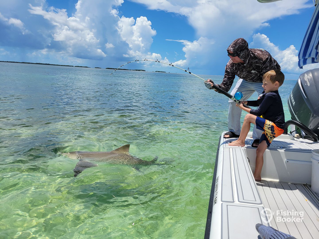 A Key West captain helps a young boy catch a Blacktip Shark from a boat in the flats on a sunny day