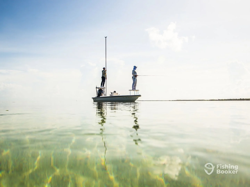 An angler stands aboard a skiff in Key West and a fishing guide stands at the back of the boat using a pole to steer and propel it across the flats on a sunny day