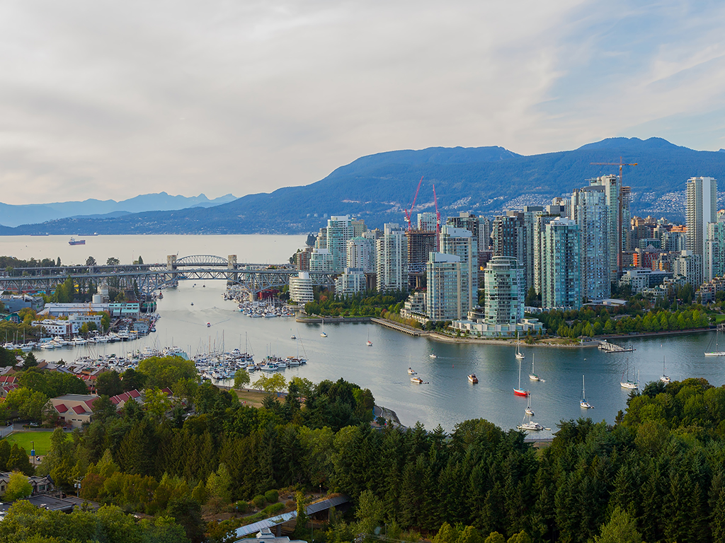 A view across the river to downtown Vancouver with small colourful fishing boats and a marina in the foreground and mountains in the background