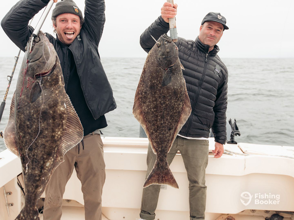 Two happy male anglers aboard a fishing charter in British Columbia each holding a Halibut on a cloudy day
