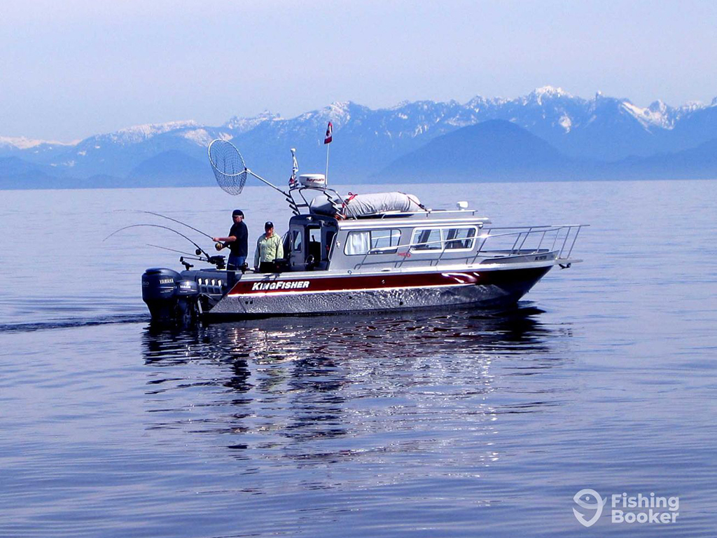 A view across the water towards anglers on a boat fish ingon a winter's day with snowy mountains in the background