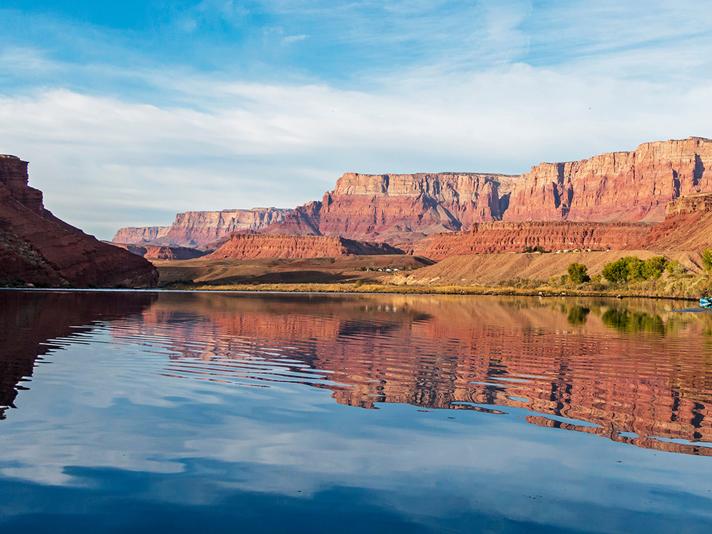 A view of the calm blue waters of the Colorado River in Arizona reflecting the red rocks visible on either side 