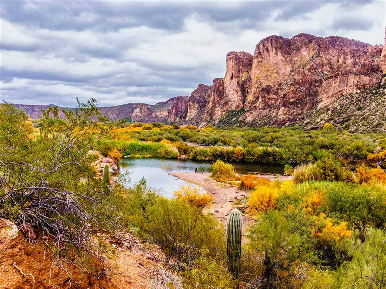 The Salt River in Arizona running past craggy rocks and cacti on a cloudy day