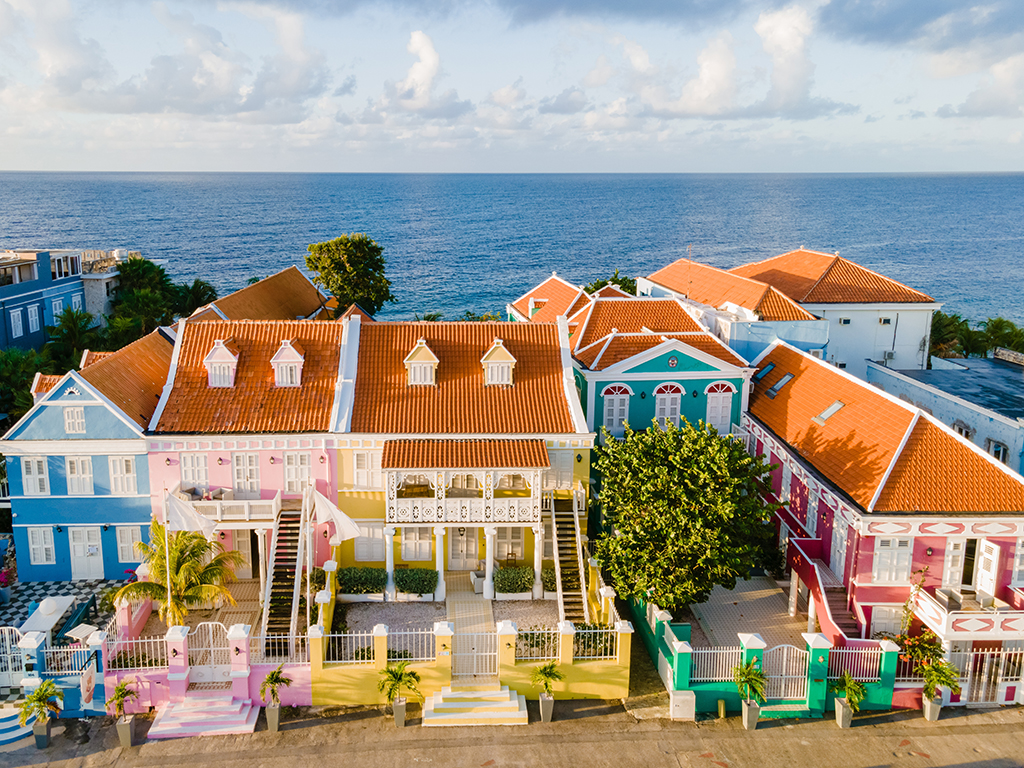 An aerial view of colorful buildings in Curaçao standing in front of a calm blue sea on a sunny day
