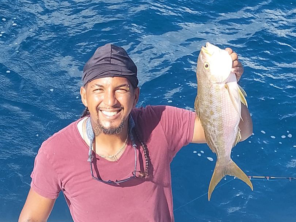 A view from above of a pleased angler holding a Snapper with calm blue open seas in the background