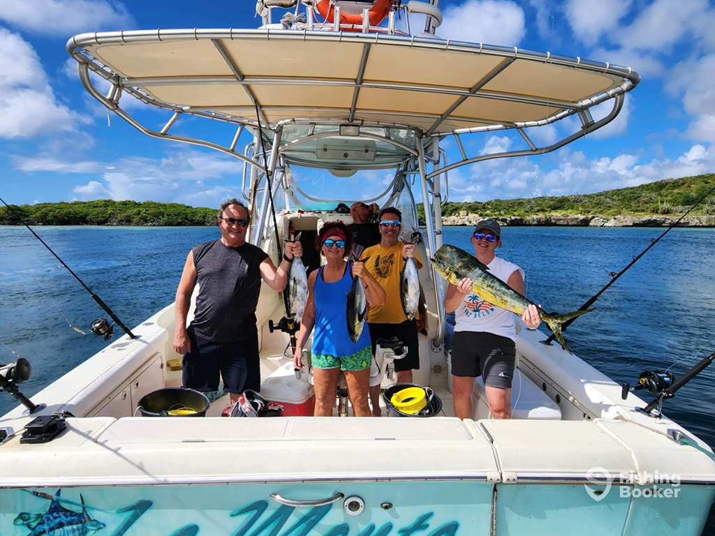 A group of happy holidaymakers stand aboard a fishing charter in Curaçao while holding colorful Mahi Mahi and Tuna