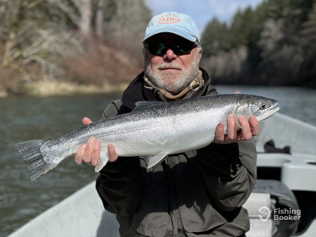 A bearded angler holds a Steelhead aboard a boat on a river in Eugene, Oregon in the winter