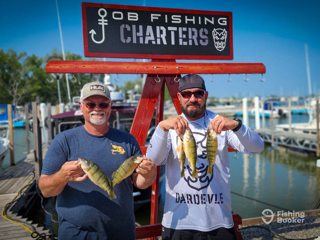 Two men stand at a fishing dock against a red guide service board holding five Yellow Perch between them on a sunny day