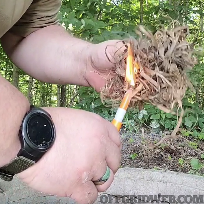 A tinder bundle being lit on fire with the flame from a sharpie marker.