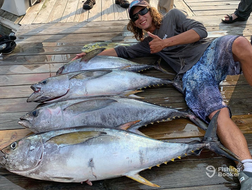 A man lies on a wooden deck in New Jersey with his thumb up next to four large Yellowfin Tuna