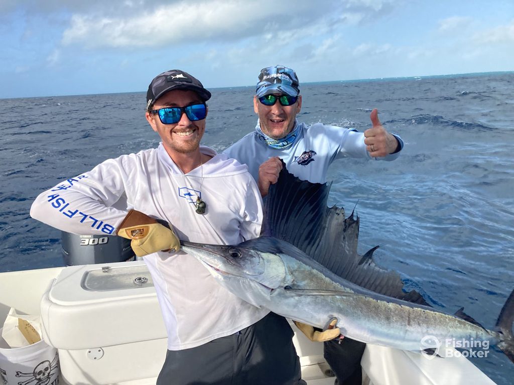 Two excited anglers stand on a boat and hold the bill and the dorsal fin of a White Marlin while wearing camouflage fishing gear