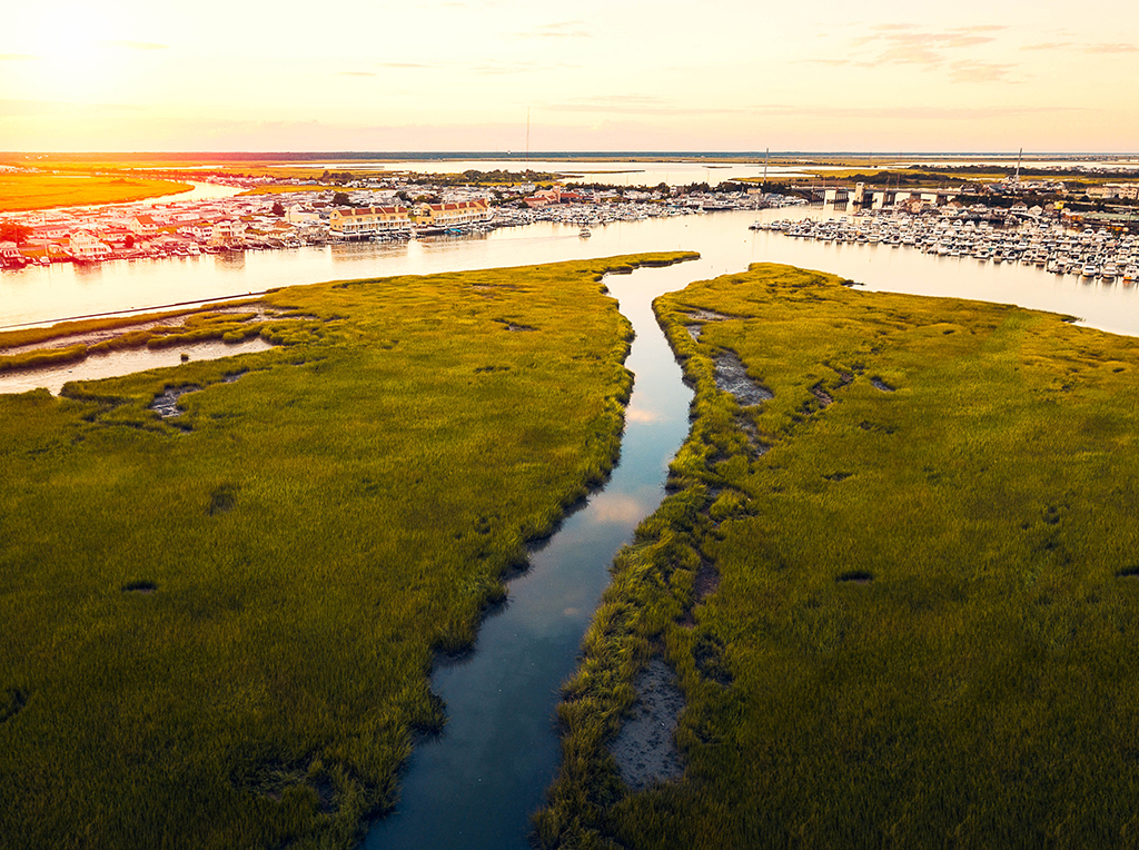 An aerial view of the bay in Wildwood, NJ as the sun is setting, with marshy islands in the foreground and houses, docks, and a marina visible on the opposite shore