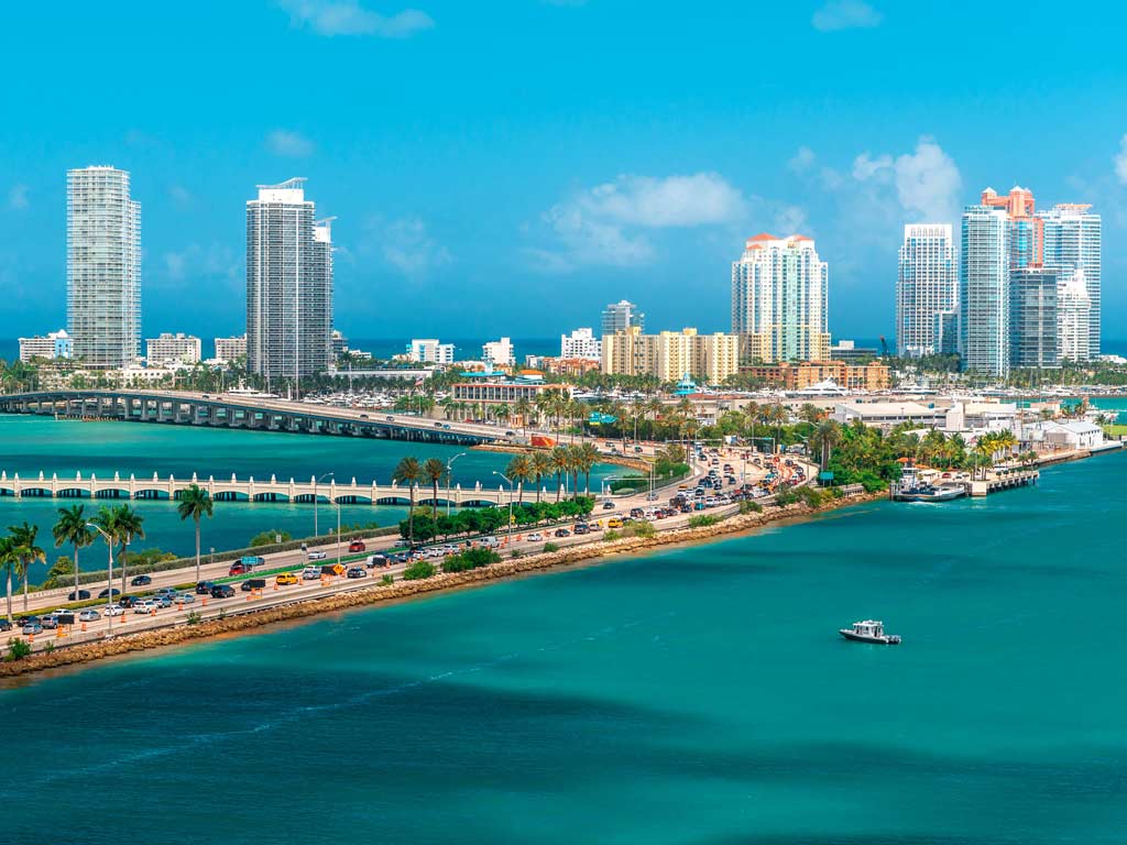 A view looking towards Miami across crystal clear blue waters on a clear day, with the city's high-rise visible in the distance