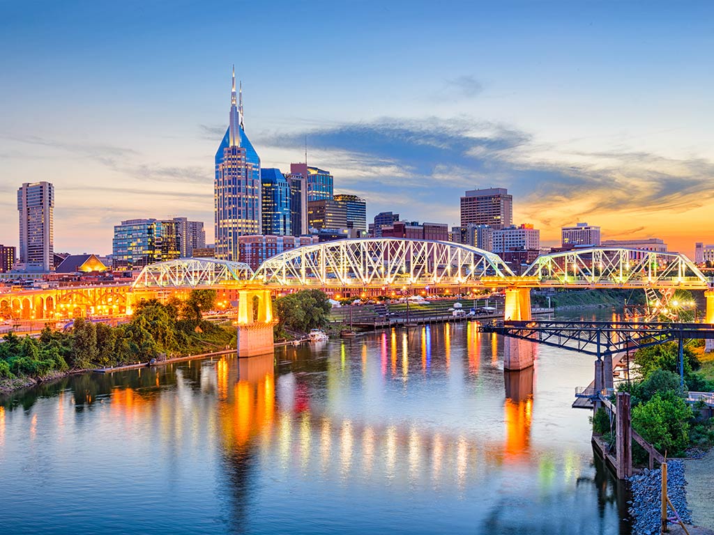 A view along the Cumberland River towards the skyline of Nashville just after sunset, with the city's famous bridge in the foreground and skyscrapers in the distance