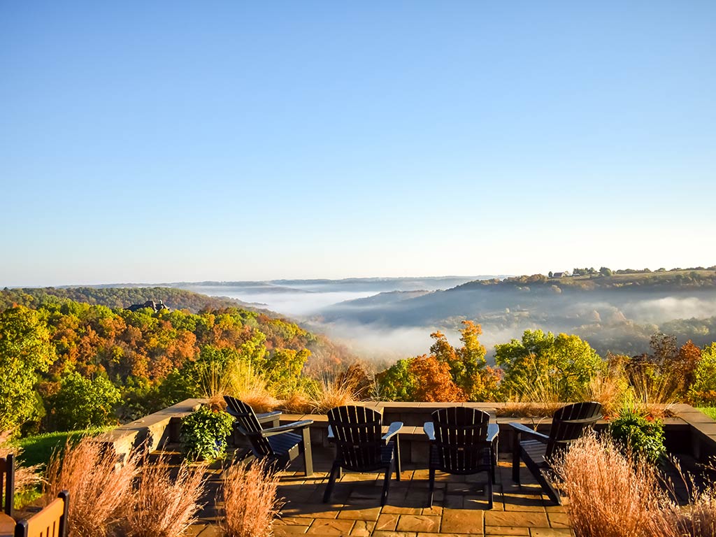 A view from a vantage point overlooking Lake of the Ozarks covered in fog on a clear morning, with early autumnal colors visible on the trees all around
