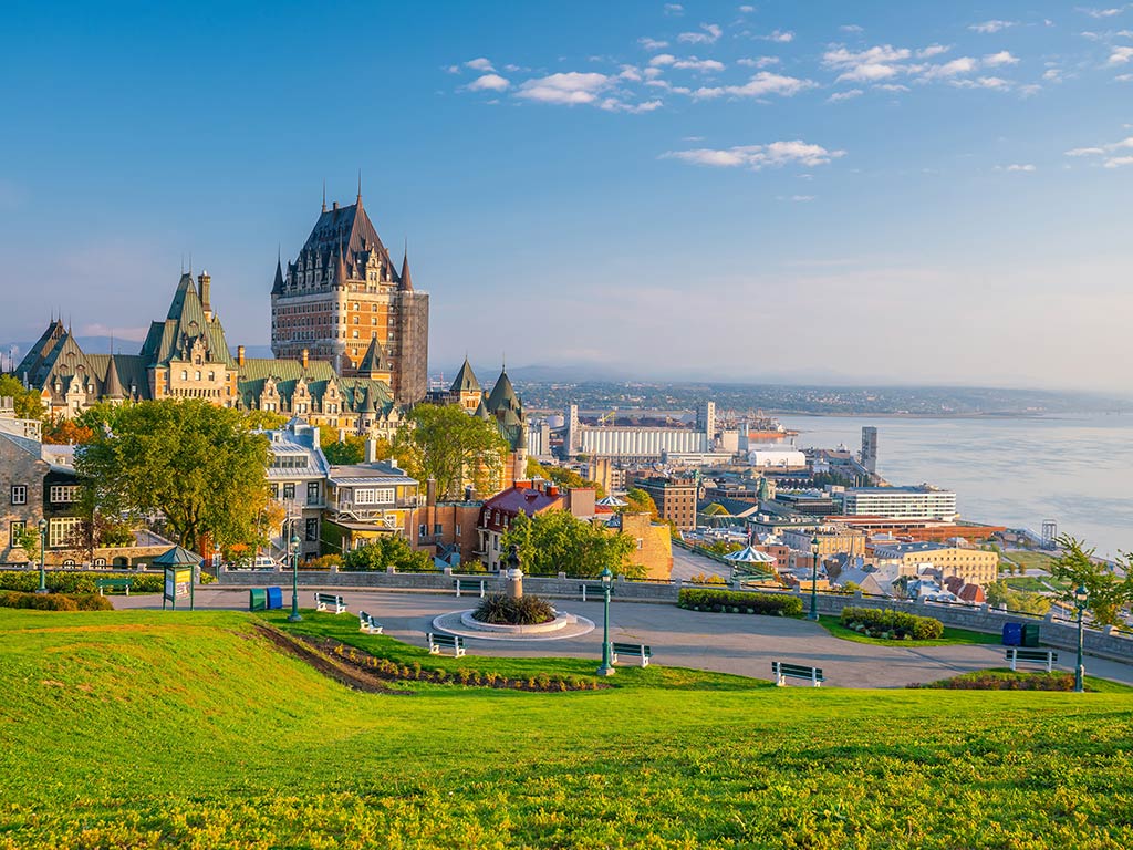 A view from a hill looking towards the St. Lawrence River in Québec City on a clear day, with the river on the right of the image and the old city centre visible across some grass on the left of the image