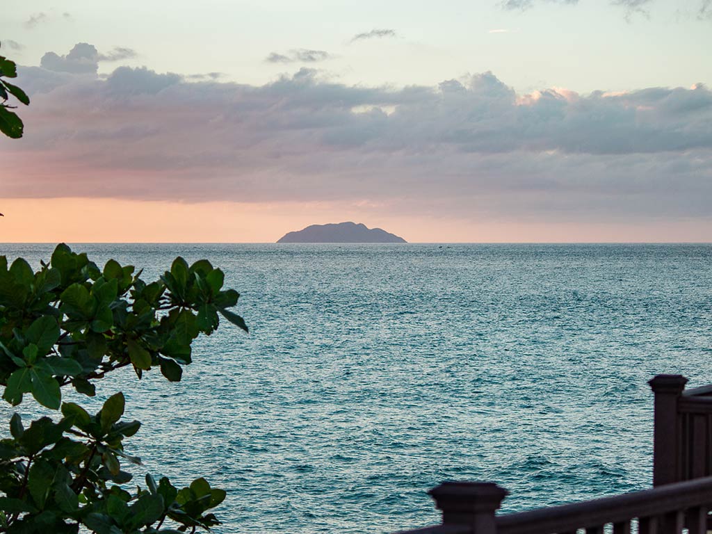 A view across the water from a boardwalk in San Juan, Puerto Rico towards the distant Desecheo Island at sunset, with some clouds visible over the island