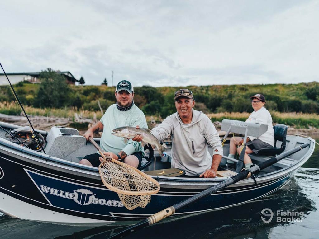 A photo of three anglers aboard a charter boat on the river; one angler is sitting in the background while two anglers are posing in front with their catch and a net