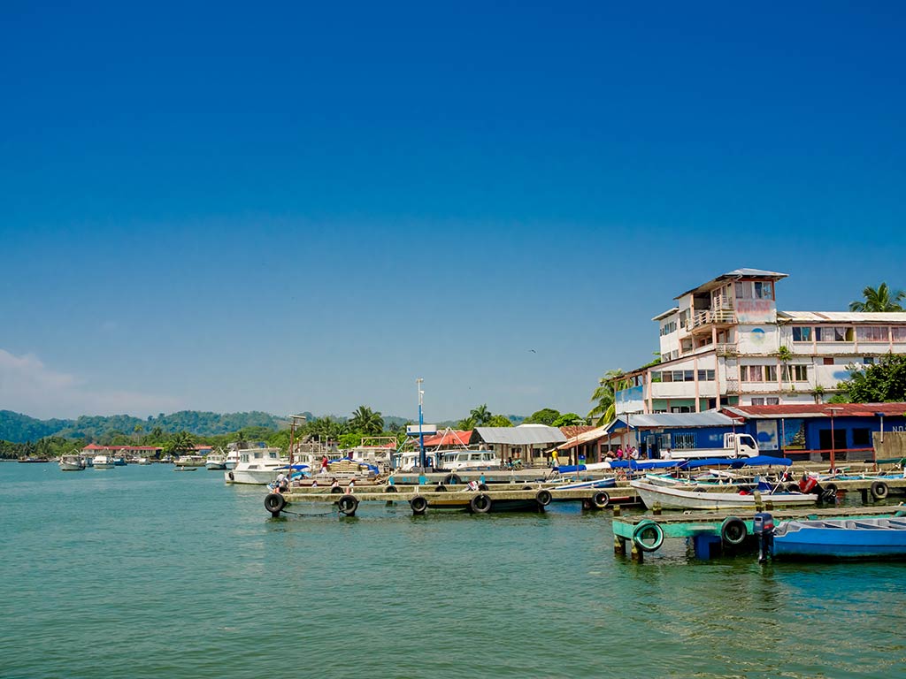 A view across the calm Caribbean waters of Livingston, Guatemala towards a small marina and some seafront buildings on a clear day