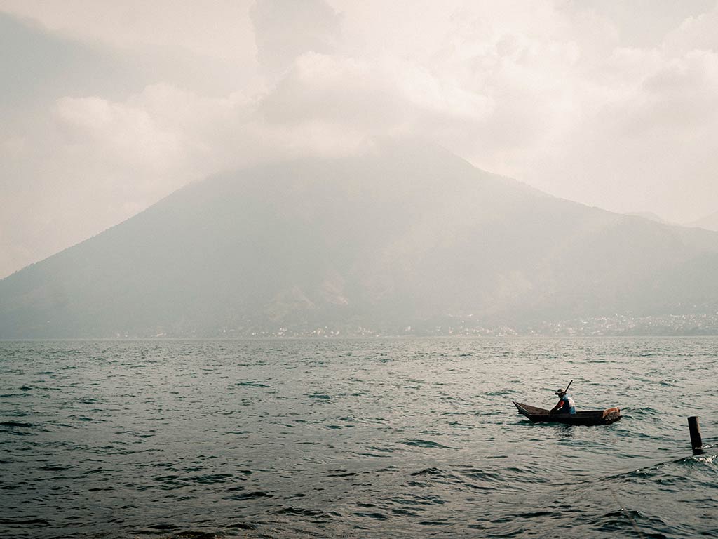 A view across the choppy waters towards a mountain on a cloudy and blustery day, with a boat in the middle of the image