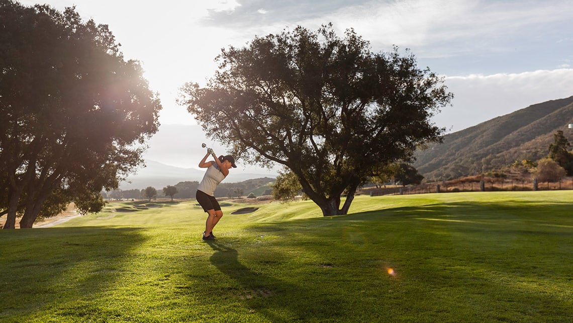 Woman golfer taking a back swing on grassy fairway.