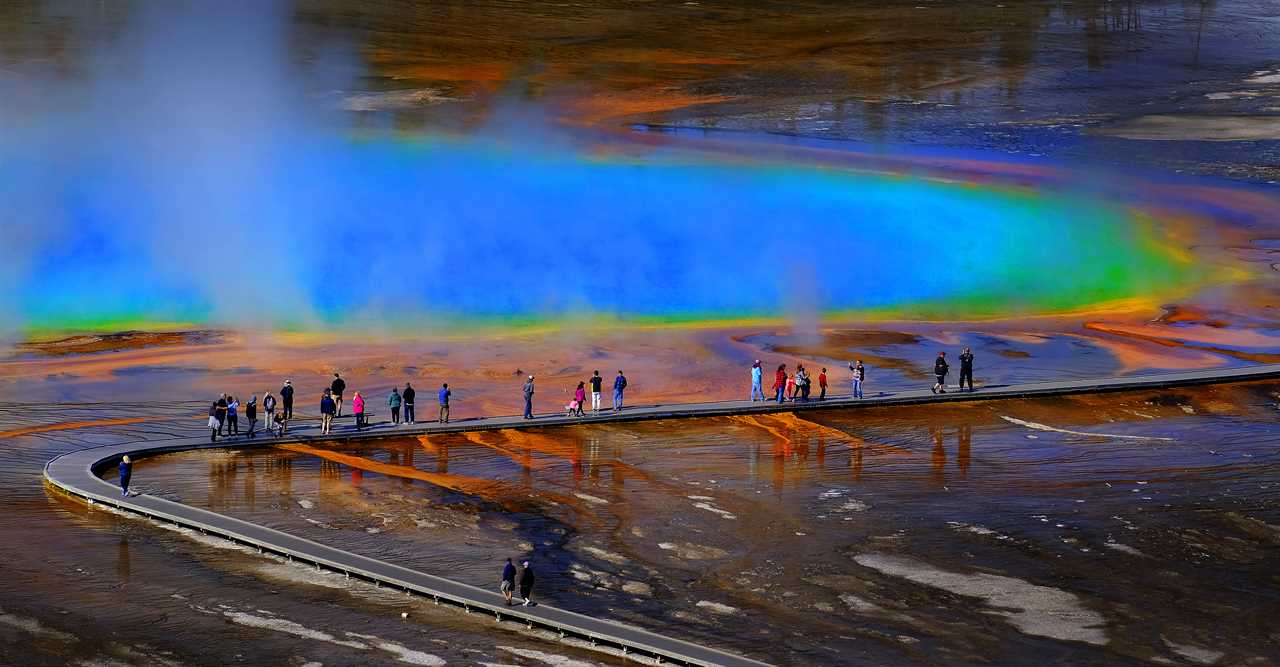 Tourists amble on a boardwalk that stretches over a volcanic spring. 