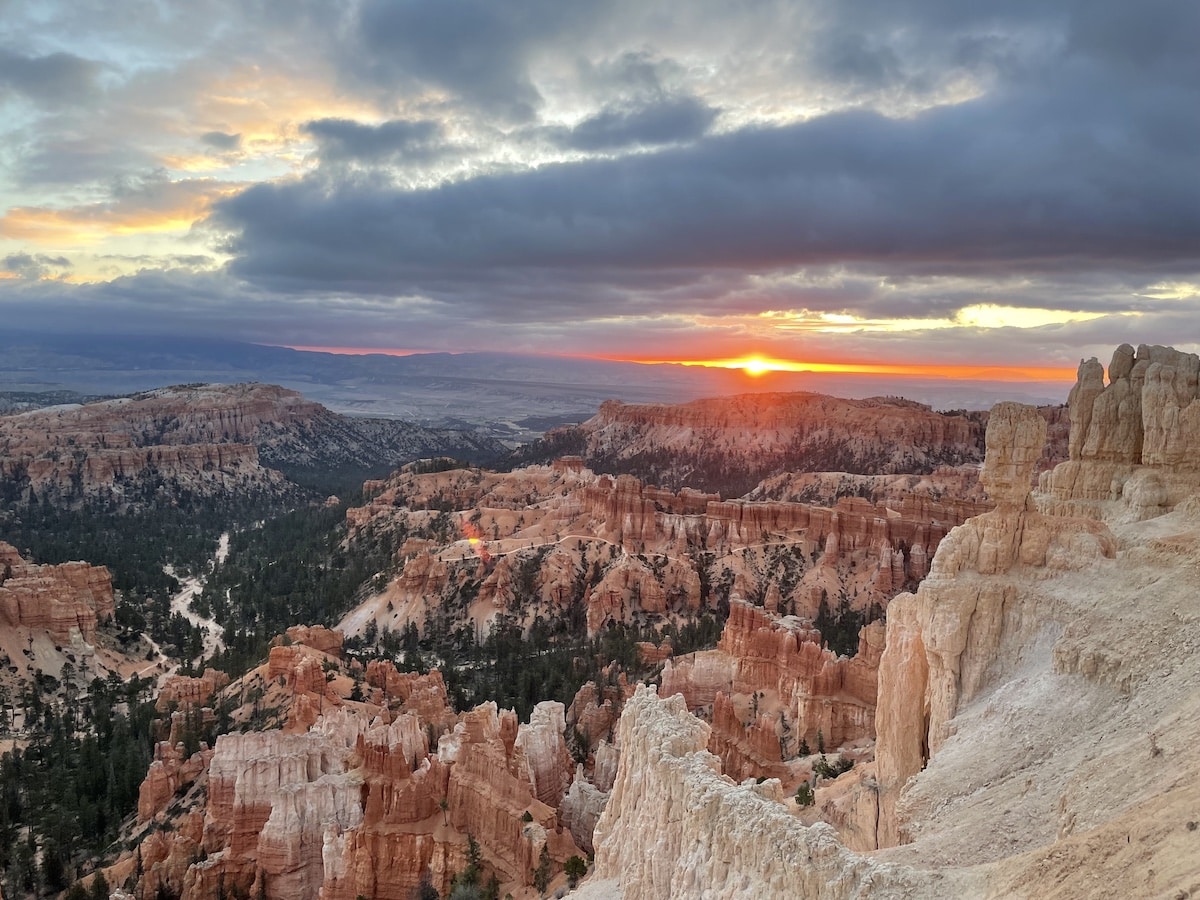 Sunrise at Inspiration Point in Bryce Canyon National Park. There is a orange and pink sun in a cloudy skies with hoodoos below.