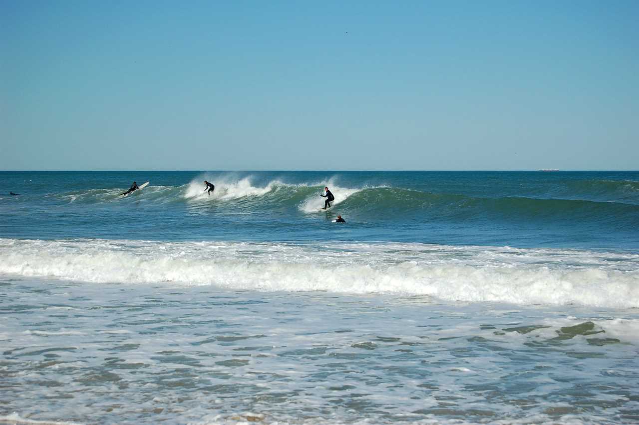 Surfers in black wetsuits ride waves into shore.