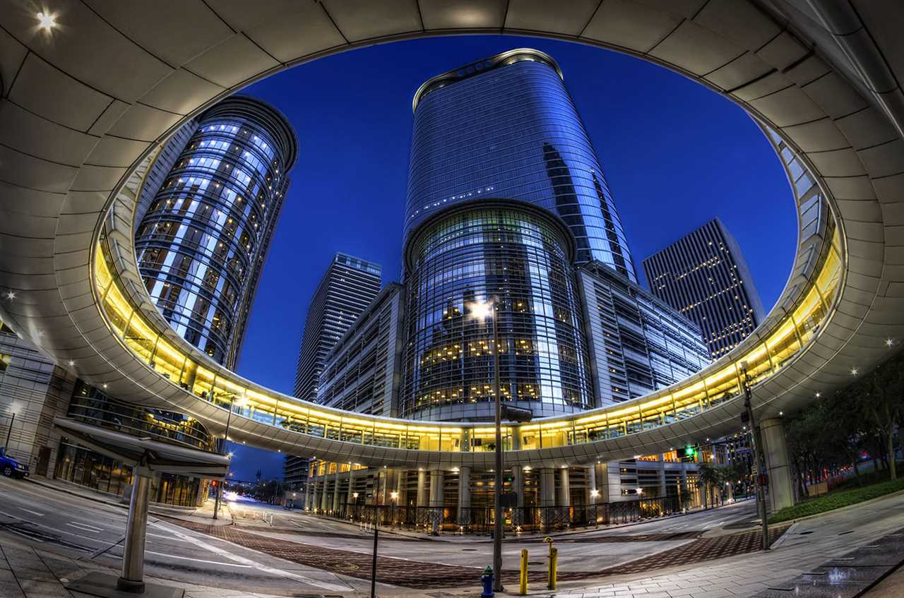 A circular walkway structure in front of gleaming skyscrapers.