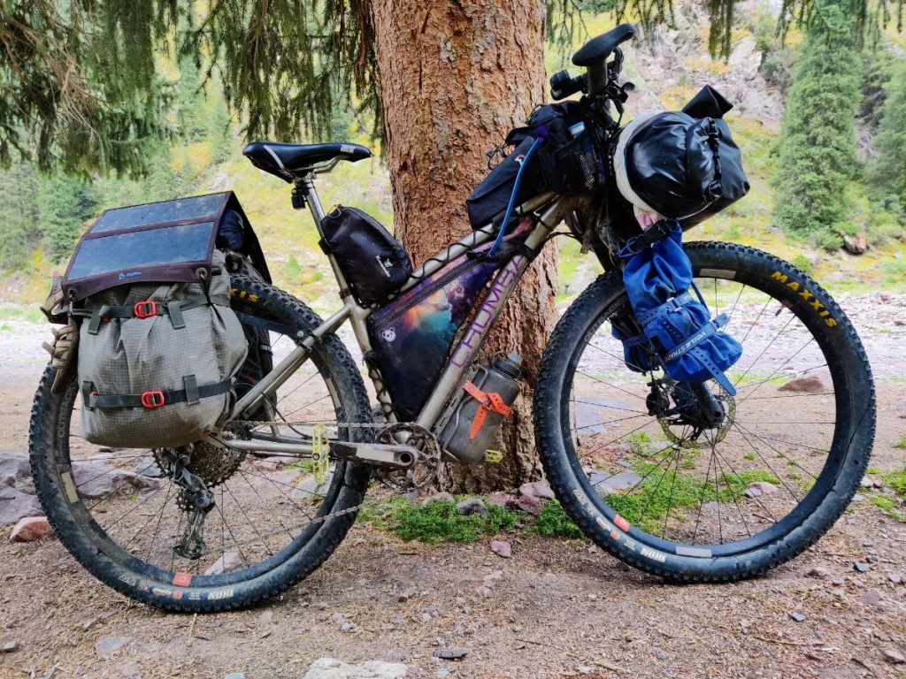 Bikepacking setup for a longer trip: rack and off-pavement panniers, fork cargo cages, and handlebar roll bag