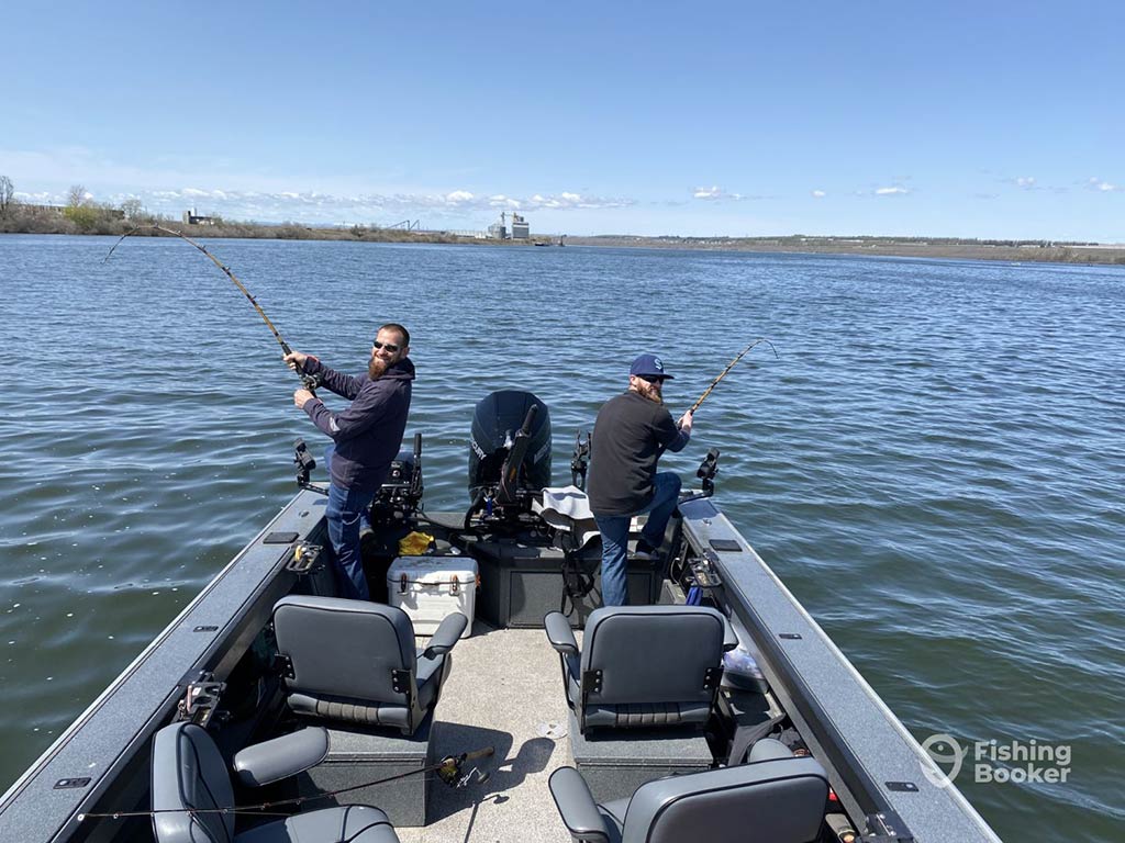 A view along a boat towards two anglers fishing into the Columbia River on a clear day, with land just about visible in the distance
