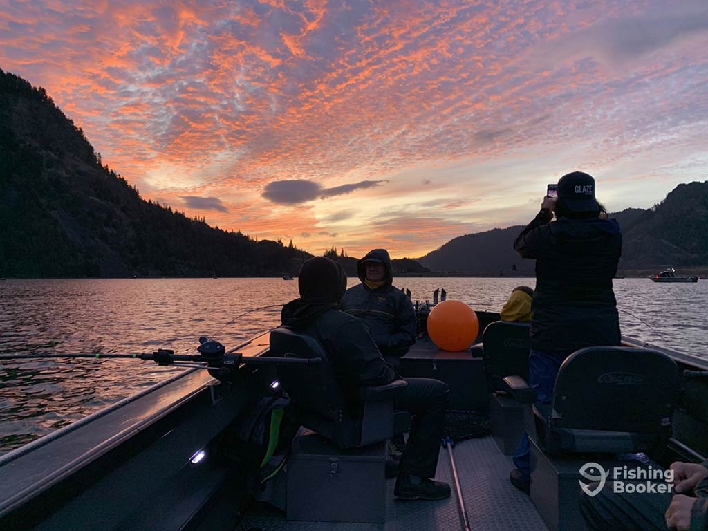 A view out the back of a fishing charter on the Columbia River at sunset, with fishing rods visible over the side of the boat and the anglers on board taking in the impressive cloud formations above
