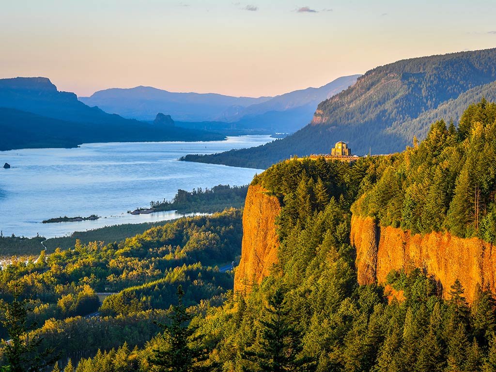 A view down the Columbia River Gorge in Oregon from a hill at sunset, with cliffs visible in the foreground and the river in the distance on a clear day