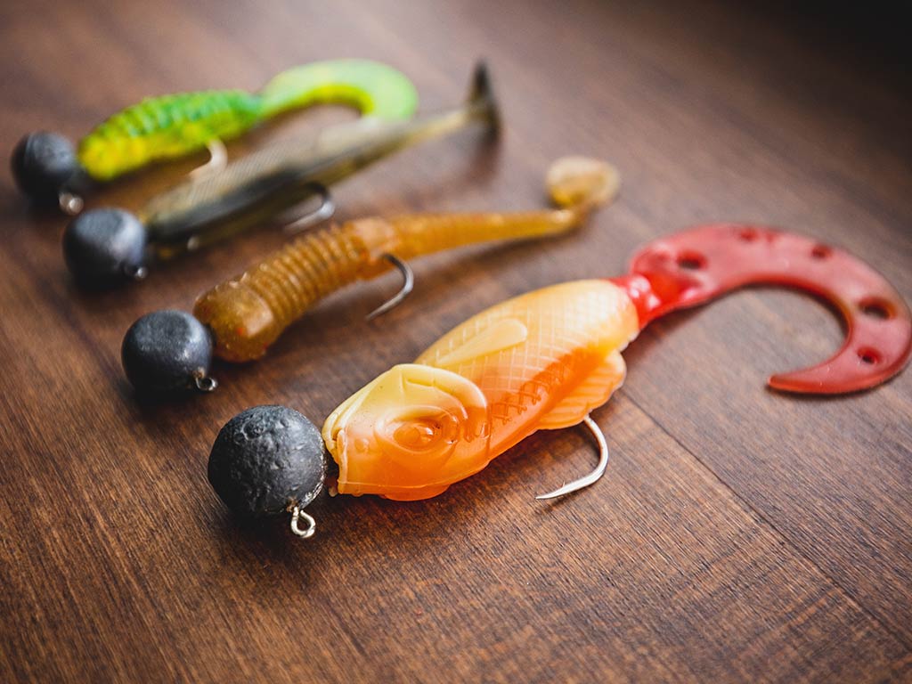 A closeup of three, brightly-colored jig-head fishing lures on a wooden table