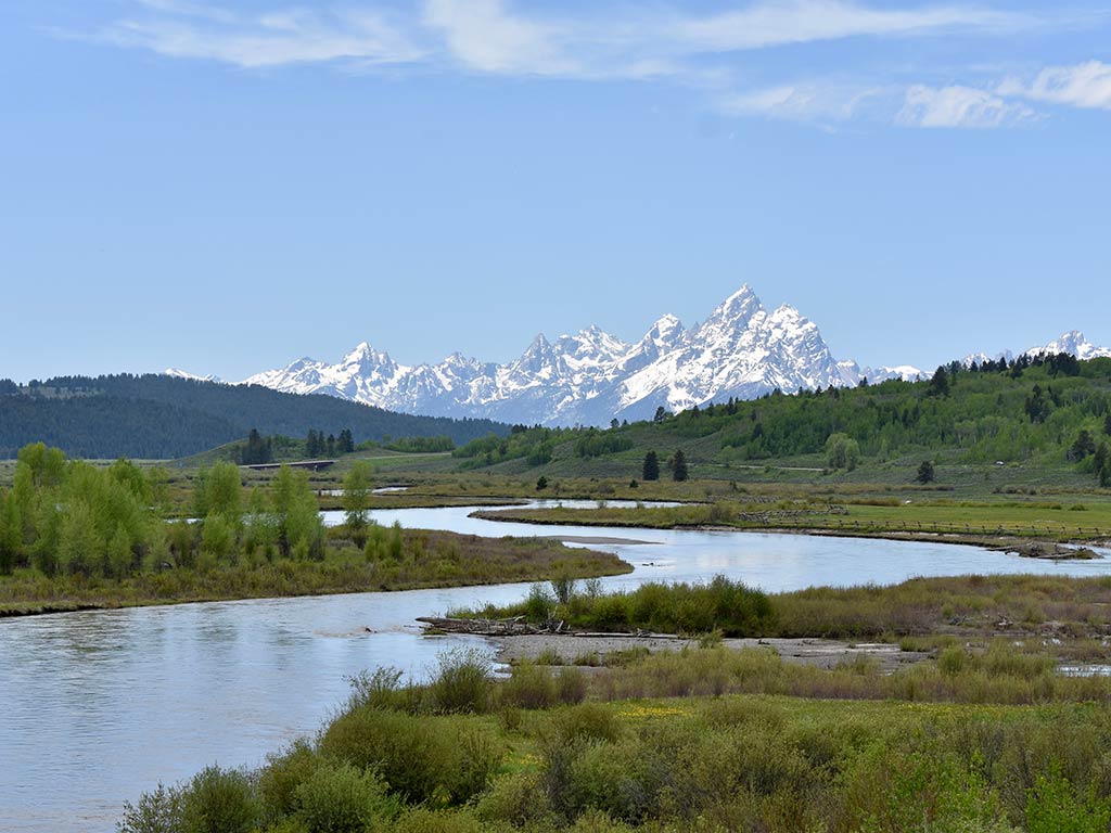 A view along the Snake River in Grand Teton National Park on a clear day, looking towards snow-capped mountain peaks along the winding waterway