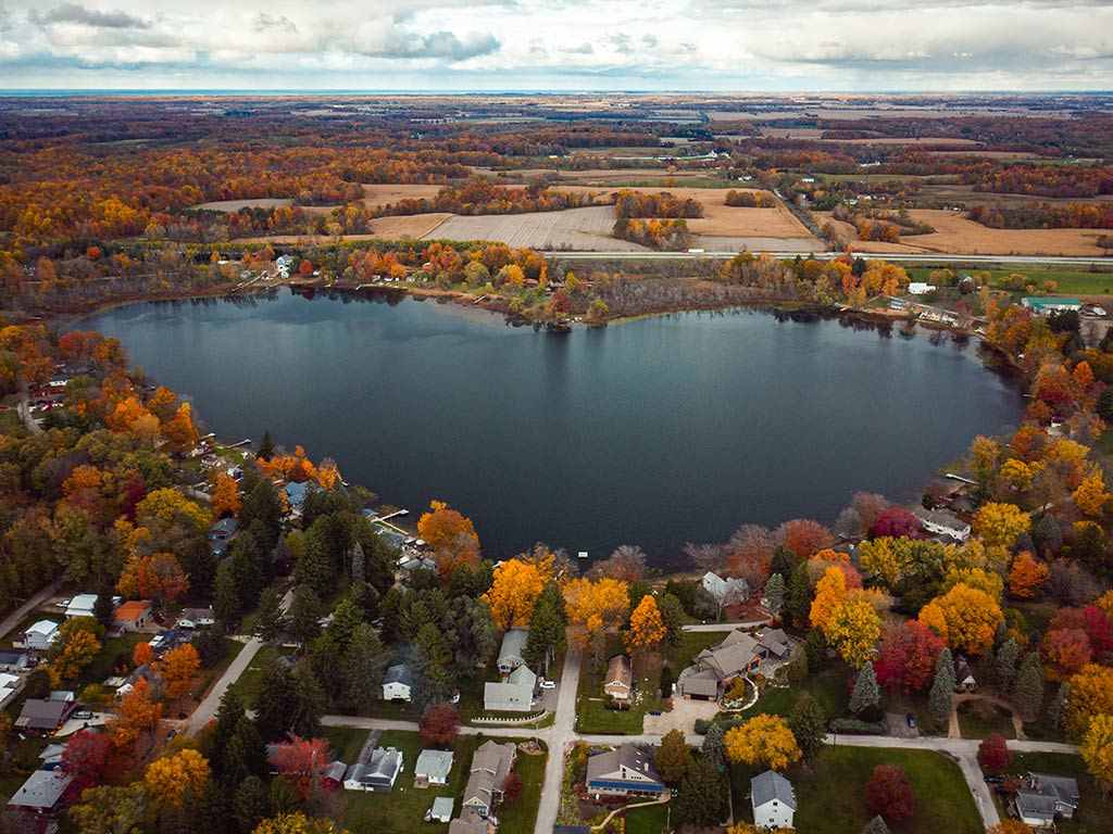 An aerial view of Saugany Lake, shaped like a heart, in Indiana during fall, with orange-brown trees visible around the shores of the water
