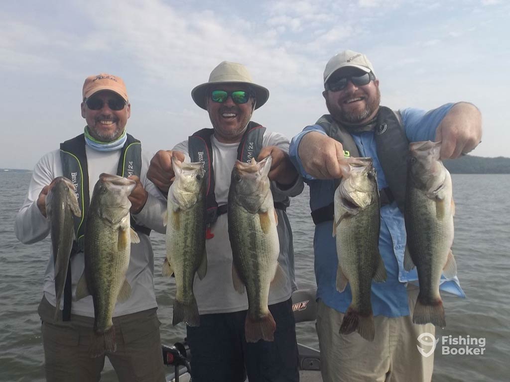 Three men in baseball caps, sunglasses, and life vests, holding up two Largemouth Basses each after a successful fishing trip in Indiana