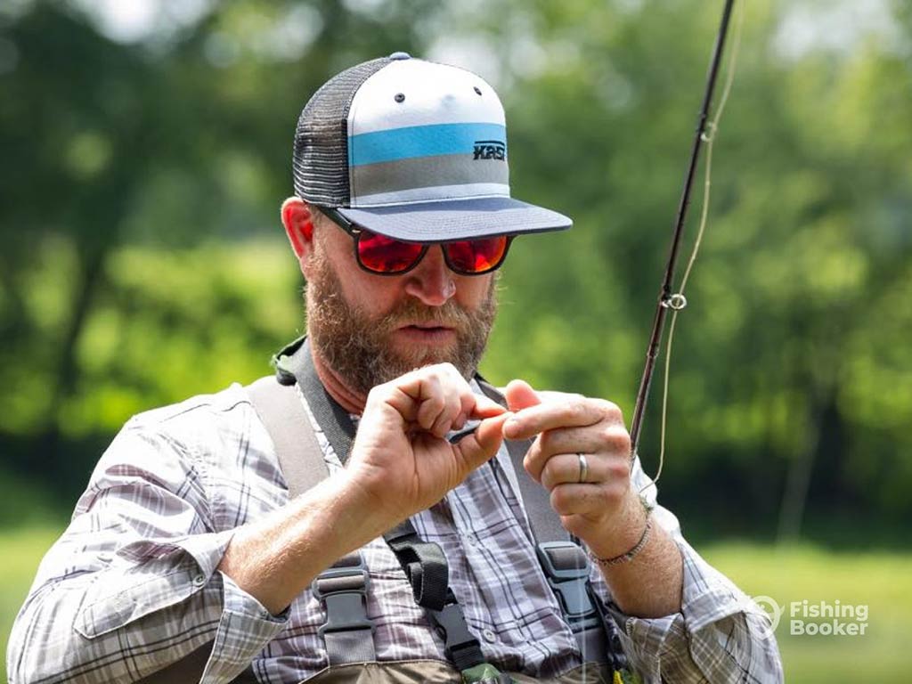 A closeup of a man in a baseball cap and sunglasses, trying to hook his fly while going fishing in Indiana in spring