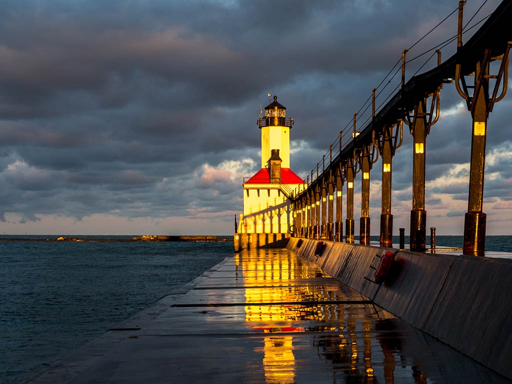 A view from the shore underneath a pier towards the Michigan City Lighthouse on Lake Michigan in Indiana on a cloudy night