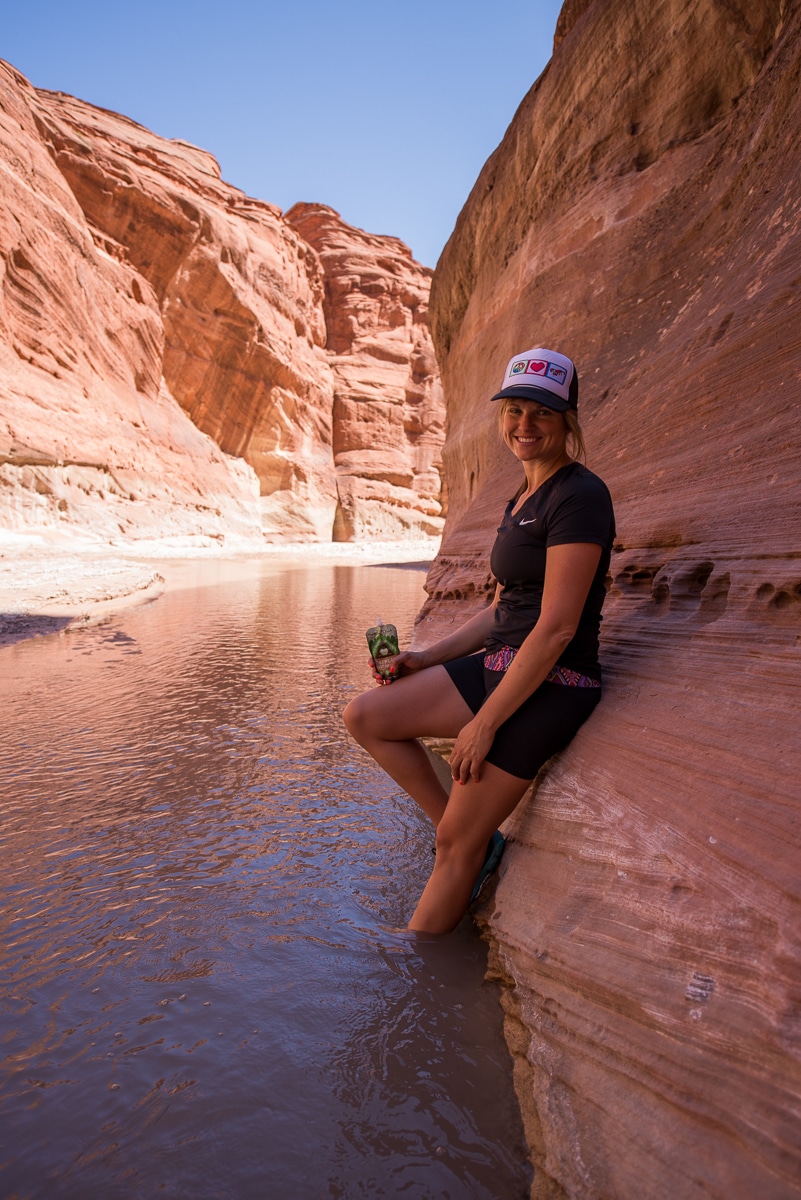 Bearfoot Theory founder Kristen Bor leaning aginst an orange canyon wall eating a snack in Paria Canyon