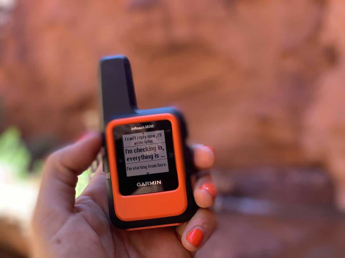 Hand holding Garmin inReach Mini GPS communication device with red rock canyon walls in background