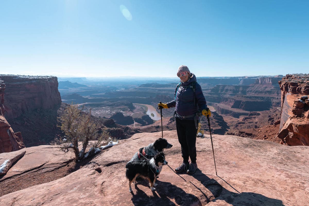 Woman with dog standing at Deadhorse Point lookout in Utah with views down into Canyonlands National Park