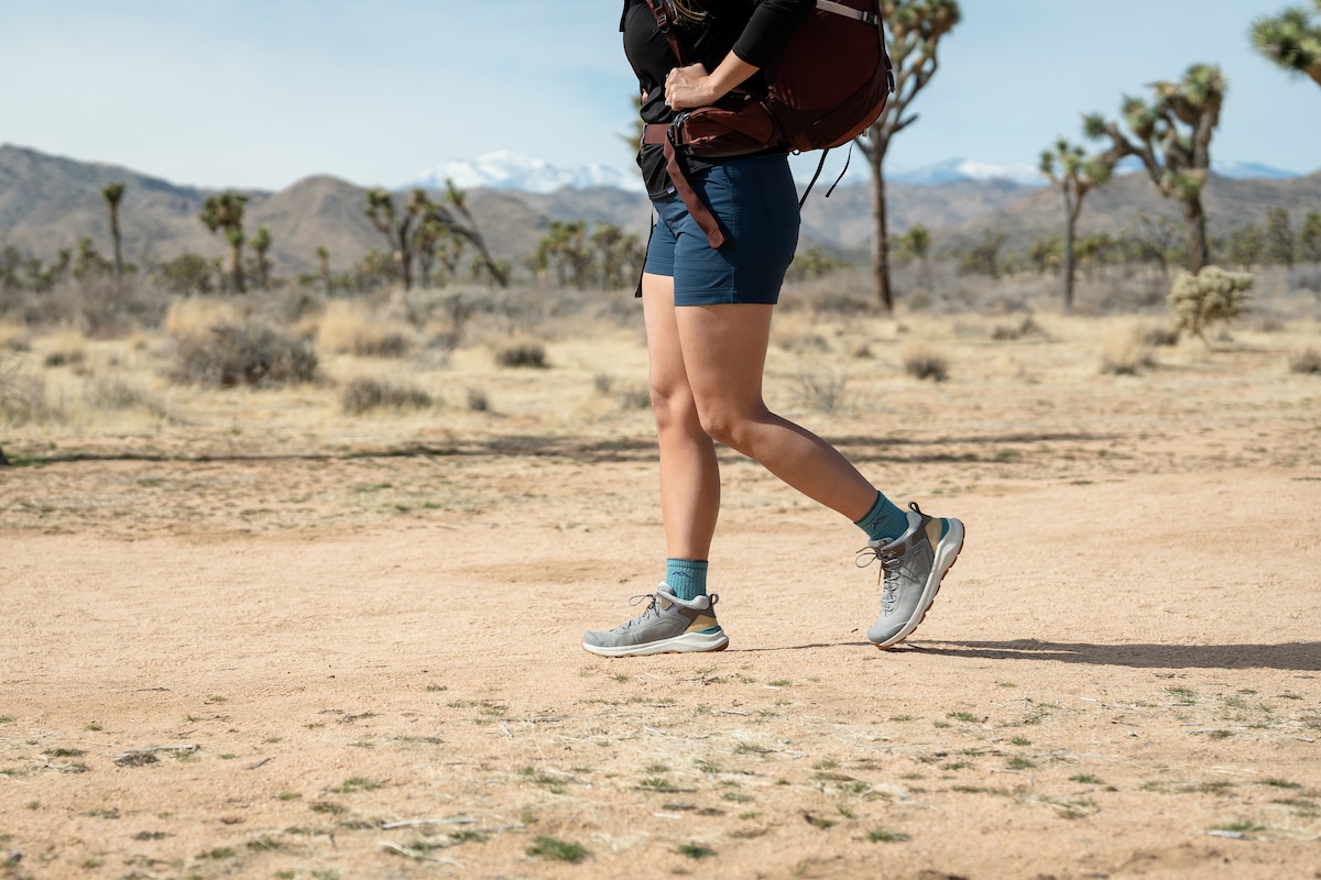 A woman carrying a backpack while wearing shorts and the Oboz Cottonwood mid waterproof hiking boots in the color Drizzle on a trail in Joshua Tree National Park