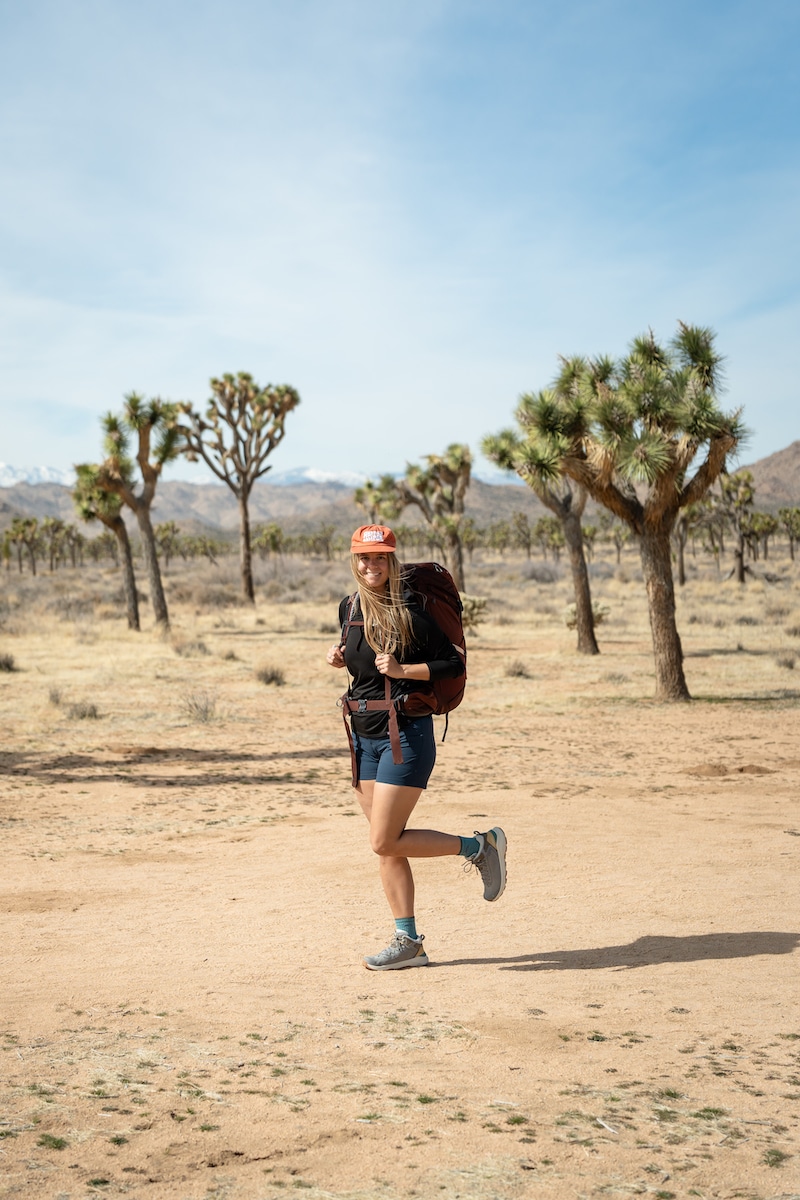 A woman backpacking while wearing shorts and the Oboz Cottonwood mid waterproof hiking boots in the color Drizzle on a trail in Joshua Tree National Park