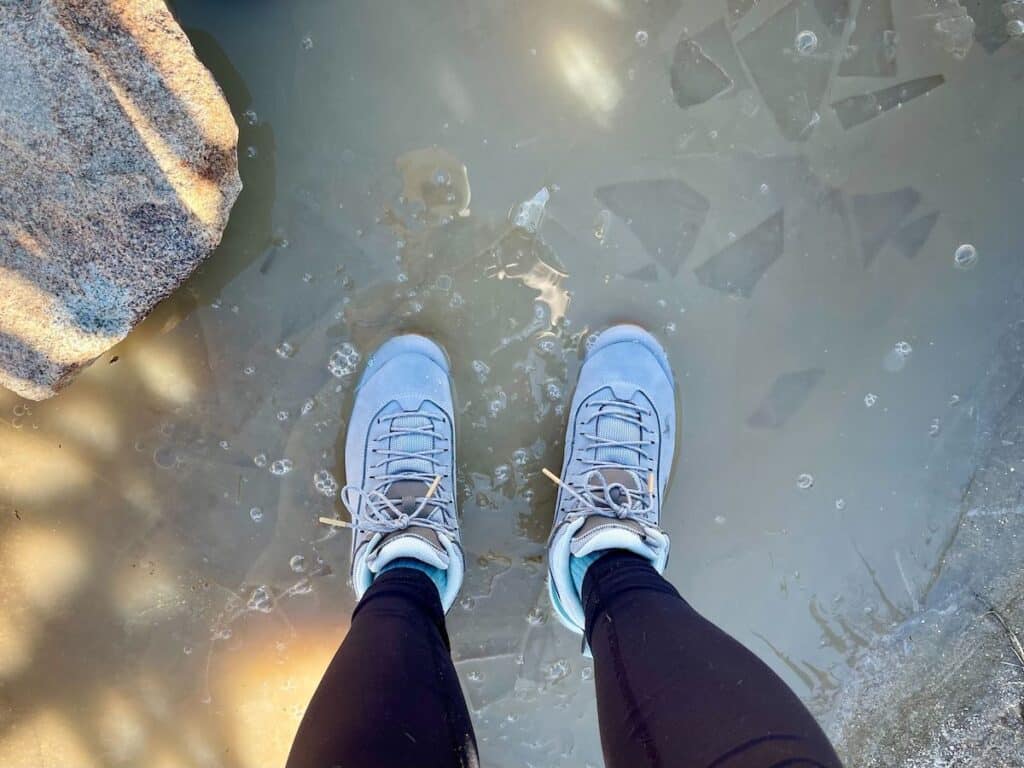 A female hiker wearing the Oboz Cottonwood mid waterproof hiking boots in the color Drizzle while standing in a puddle in Joshua Tree National Park