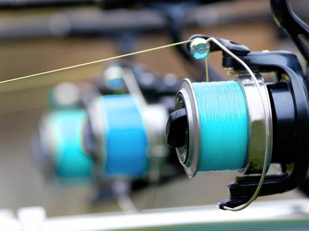 A closeup of one spin fishing reel wound tight with a blue line, with two similar reels out of focus in the background