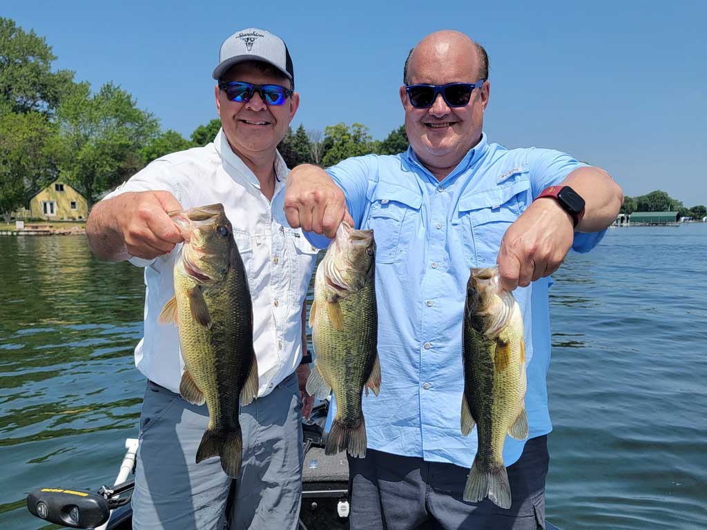 A photo of two anglers standing on a charter fishing boat and posing with three decent Bass catches landed in the peak of summer