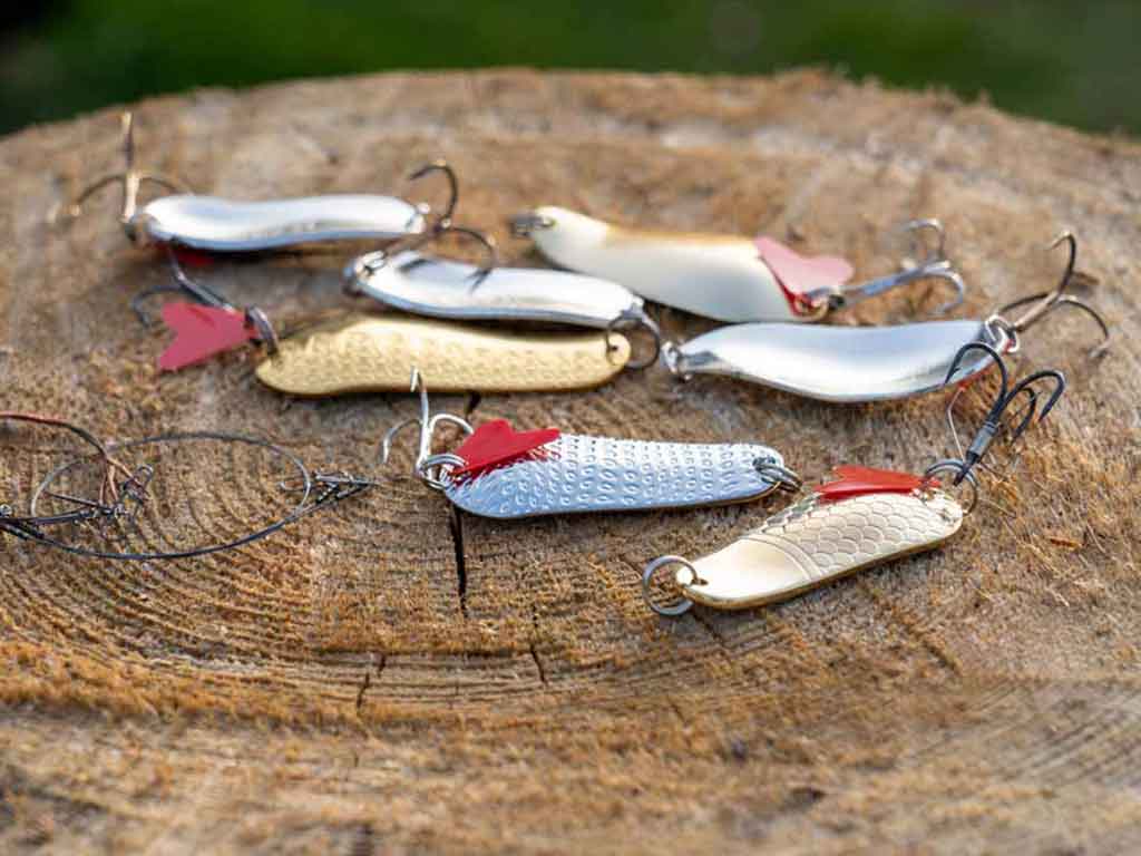 An assortment of colorful spoon lures for river fishing laid out on a stump of a tree