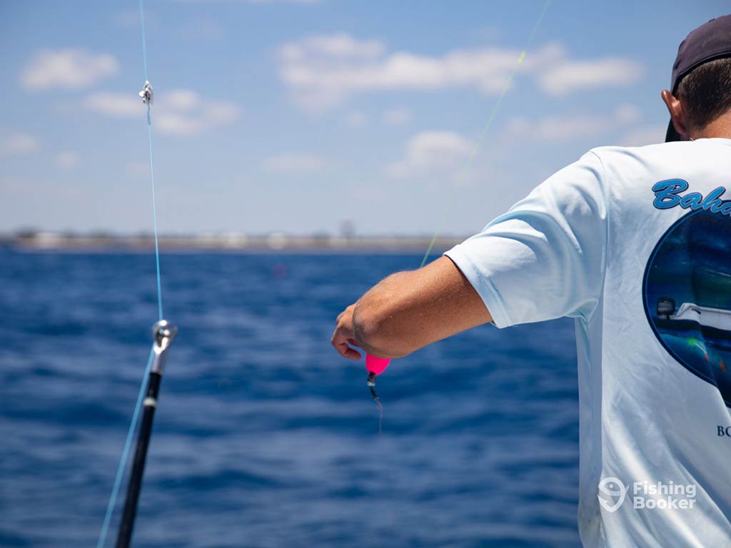 A view from behind of an angler as he sets up a lure on a fishing line to troll in Florida, with the ocean waters visible around him and land blurry in the distance
